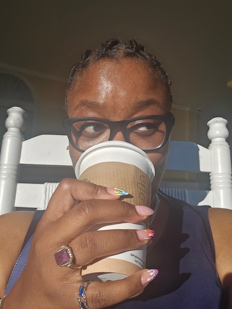 Me sipping coffee with medium box braids slicked back into a ponytail that isn't visible behind my head. 